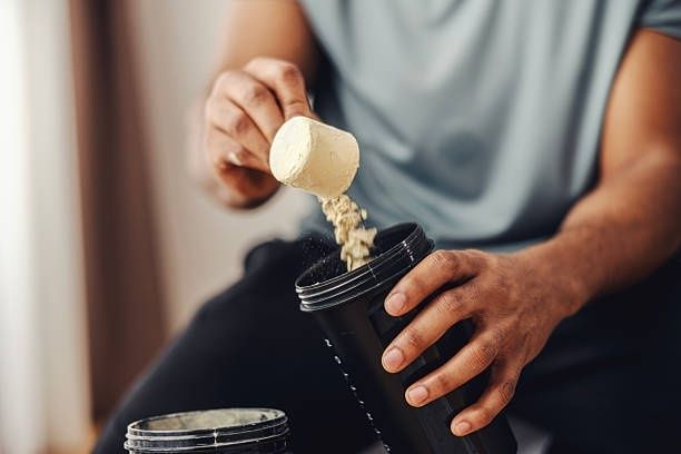 Persoon doet een schep eiwitpoeder in een zwarte shaker