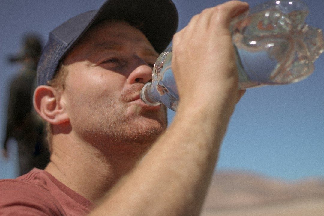 Sportieve man drinkt water uit een grote plastic fles in de zon